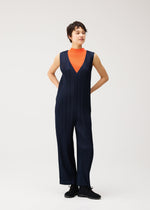 A person stands with hands behind their back against a plain light background, wearing the PLEATS PLEASE ISSEY MIYAKE THICKER BOTTOMS 2—a sleeveless navy blue V-neck jumpsuit featuring pockets and a sharply pleated front, layered over an orange turtleneck. Crafted from thick fabric, this structured outfit exudes modern sophistication.