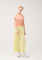 A woman with light skin and red hair models the MONTHLY COLORS : JULY sleeveless shirt and wide-leg pants by PLEATS PLEASE ISSEY MIYAKE, paired with white high-top sneakers against a plain light background.