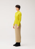 Person standing in profile against a plain background, wearing the MONTHLY COLORS : OCTOBER by PLEATS PLEASE ISSEY MIYAKE—a bright yellow long-sleeved, high-neck top and beige pleated skirt with black shoes.