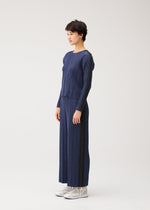 A woman in profile models the COTTON DENIM round-neck top and wide-leg pants by PLEATS PLEASE ISSEY MIYAKE with white lace-up shoes, set against a plain white background.