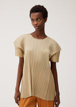 A person wears the beige, floral-inspired BOUQUET top by PLEATS PLEASE ISSEY MIYAKE with orange pants, standing against a plain light background and looking slightly to the side with a neutral expression.