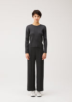 A person stands against a plain light background, wearing PLEATS PLEASE ISSEY MIYAKE COTTON DENIM BLACK with matching wide-leg pants and white lace-up shoes.