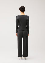 A person with short dark hair faces away, wearing the COTTON DENIM BLACK set by PLEATS PLEASE ISSEY MIYAKE and white sneakers against a plain light background.