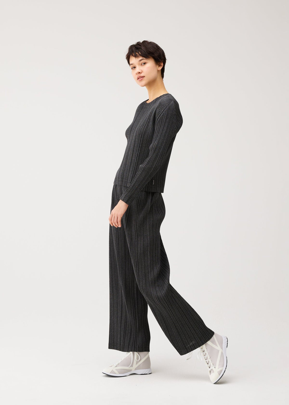 Zoomed view A person poses casually in the COTTON DENIM BLACK set by PLEATS PLEASE ISSEY MIYAKE with white high-top sneakers against a plain white background.
