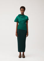A woman with short curly hair wears the LEAP top and skirt from PLEATS PLEASE ISSEY MIYAKE in green, featuring pleats, an asymmetrical silhouette, short sleeves, and pairs them with neutral brown shoes.