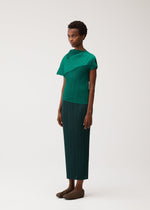 A person wears the LEAP set by PLEATS PLEASE ISSEY MIYAKE: a dark green, short-sleeved pleated top with an asymmetrical silhouette, matching long skirt, and brown shoes against a plain background.