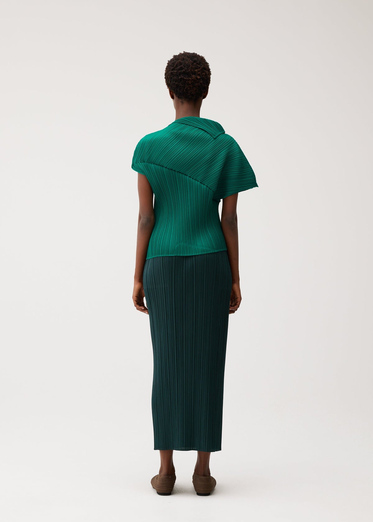 Zoomed view A person faces away, wearing the LEAP green pleated top and matching long skirt by PLEATS PLEASE ISSEY MIYAKE against a plain light background.