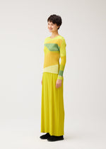 A person models the ORBIT set by PLEATS PLEASE ISSEY MIYAKE—featuring a long, pleated yellow skirt and a matching yellow-green, round-neck long-sleeved top—against a plain white background.