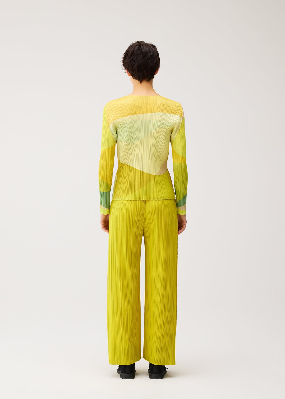 Zoomed view A person with short dark hair faces away, wearing the ORBIT round-neck pleated top and matching wide-leg pants by PLEATS PLEASE ISSEY MIYAKE; black shoes and a plain light background complete the look.
