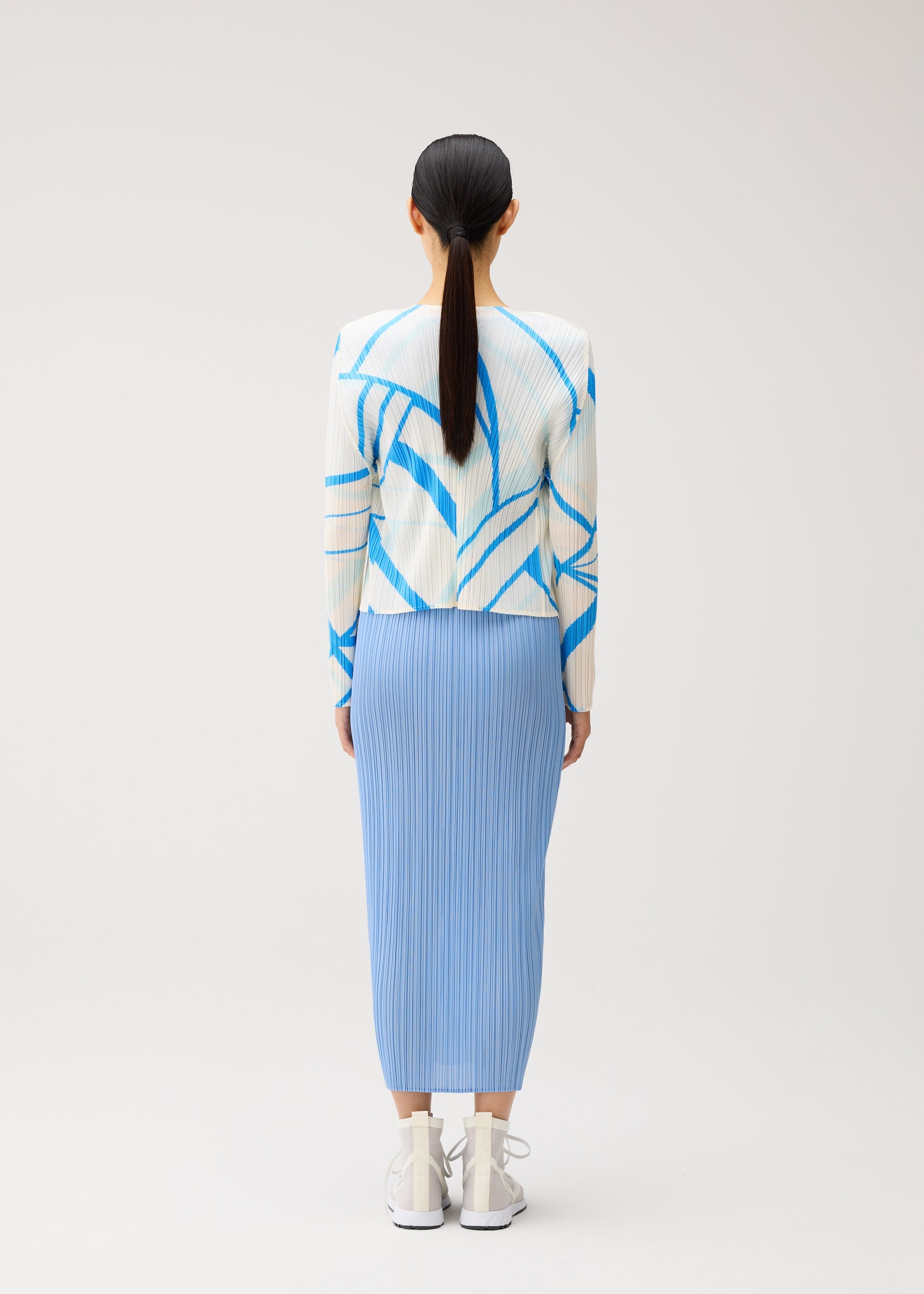 Zoomed view A person with long dark hair in a ponytail, dressed in the FOLD LINE sweater by PLEATS PLEASE ISSEY MIYAKE—featuring white and blue geometric patterns inspired by minimalist design—paired with a light blue pleated skirt and white sneakers, stands facing away against a plain light background.