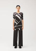 A person stands facing forward, dressed in the PLEATS PLEASE ISSEY MIYAKE FOLD LINE tunic featuring a black and white geometric pattern with a round neckline, paired with wide black pleated pants and black shoes, exemplifying minimalist design against a plain light background.