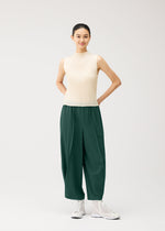 Wearing the PLEATS PLEASE ISSEY MIYAKE A-POC BOTTOMS, a person in a sleeveless beige top and white sneakers stands against a plain light background, smiling with their hands behind their back.