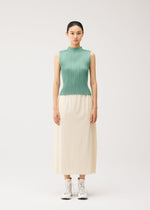 A woman stands facing forward, wearing a sleeveless green pleated top and PLEATS PLEASE ISSEY MIYAKE A-POC BOTTOMS—a long cream skirt with pockets—paired with white lace-up boots, against a plain light background.