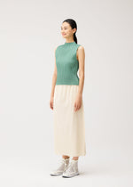 A woman stands against a plain light background, wearing PLEATS PLEASE ISSEY MIYAKE’s A-POC BOTTOMS—a cream pleated skirt—paired with a green sleeveless top and white high-top sneakers.