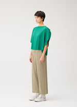 A person stands in profile against a plain background, wearing the PLEATS PLEASE ISSEY MIYAKE A-POC SLICE top, paired with wide-leg beige pleated pants and white lace-up shoes.