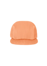 The PLEATS CAP by PLEATS PLEASE ISSEY MIYAKE is peach-colored with pleats, a soft ribbed texture, and a wide structured brim, shown against a white background.