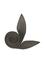 The MONTHLY SCARF AUGUST by PLEATS PLEASE ISSEY MIYAKE is a coiled, pleated, dark gray, diamond-shaped scarf with two pointed ends, arranged on a white background to resemble a stylized snail with leaf-like antennae. - CHARCOAL （no.17）