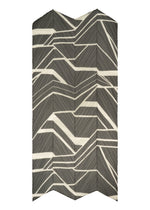 The FOLD LINE SCARF by PLEATS PLEASE ISSEY MIYAKE features a dynamic, modern chevron motif with black, white, and gray angled lines in a geometric zigzag pattern reminiscent of diagonal gift wrapping.
