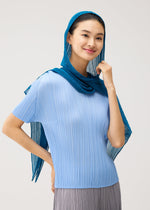 A woman wearing a light blue pleated top and the FOLD HOOD SCARF by PLEATS PLEASE ISSEY MIYAKE smiles as she touches her chin. Set against a plain, light background, her stylish pleated scarf from PLEATS PLEASE ISSEY MIYAKE adds an elegant touch to her ensemble.