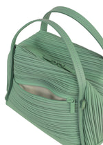A close-up of the BIAS PLEATS BAG by PLEATS PLEASE ISSEY MIYAKE shows its light green color, two handles, and a zippered outer pocket. The diagonal pleating creates a ribbed texture that gives the bag a unique, stylish look.