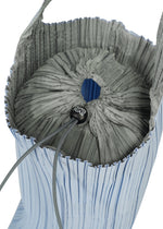 A close-up of the PLEATS SWAN BAG by PLEATS PLEASE ISSEY MIYAKE reveals its pleated design and drawstring closure, highlighted by a black toggle with white text. This elegant handbag boasts a light blue exterior and gray interior, seamlessly blending style and functionality in one sophisticated accessory.