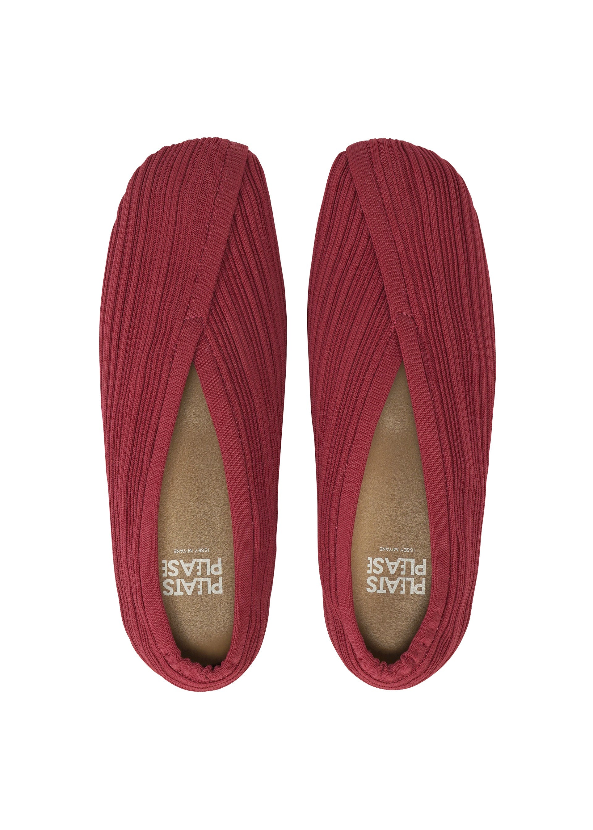 Zoomed view A pair of red KNIT BALLET SHOES by PLEATS PLEASE ISSEY MIYAKE, seen from above, showcase a pleated, knitted fabric texture and a subtly pointed toe. The insoles are marked with “PLATS PLEASE” in white lettering.