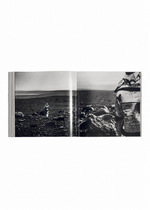 Open book from ISSEY MIYAKE (Limited Collectors Edition) by ISSEY MIYAKE BOOKS, featuring a black-and-white photograph of a stark, rocky landscape. On the left page, a solitary figure stands in the distance, while another person—partially seen and turned away—appears on the right page. The composition echoes Issey Miyake’s distinctive design philosophy and invites thoughtful contemplation, making this edition a striking Collector’s piece.