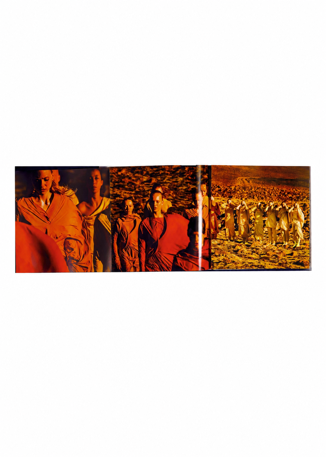 A group of people dressed in earth-toned outfits, reflecting the design philosophy behind the ISSEY MIYAKE (Limited Collectors Edition) from ISSEY MIYAKE BOOKS, walk across a rocky, orange-lit landscape. The scene is divided into three vertical panels, producing a sequential visual effect. view 12 of 17