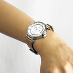 A close-up of a wrist wearing the ISSEY MIYAKE WATCH "W mini by Satoshi Wada," featuring a gauge-inspired dial, silver casing, white face, blue hands, and tan leather strap against a plain white background.